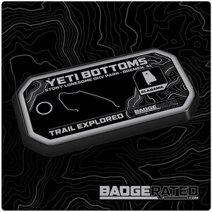 May include: A black and white rectangular badge with the text "YETI BOTTOMS" and "TRAIL EXPLORED". The badge features a map of Alabama and the text "STONY LONESOME OHV PARK - BREMEN, AL". The bottom of the badge has the text "BADGERATED.COM".