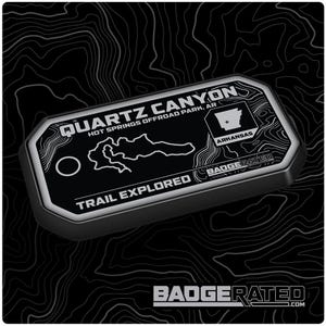 May include: A black and silver metal badge with the text "Quartz Canyon Hot Springs Offroad Park, AR" and "Trail Explored". The badge also features a map of the park and the state of Arkansas with a star.