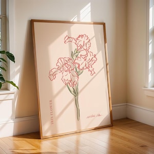 May include: A framed art print featuring a pink iris flower illustration on a light peach background. The print includes the text "IRIS FLOWER" and a signature. The frame is a light brown color.