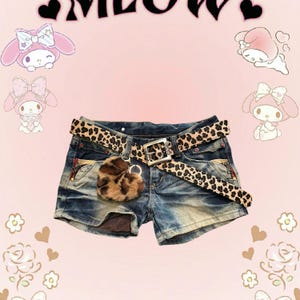 May include: Blue denim shorts with a leopard print belt and a fluffy leopard print heart-shaped keychain. The shorts have distressed details and multiple pockets.