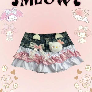 May include: Denim skirt with white and pink frilled layers, decorated with a Hello Kitty plush and cat ears. Features a bow with lace detailing. The background includes cartoon characters and the word "MEOW".