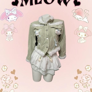 Puede incluir: Una chaqueta vaquera verde claro con ribete de piel sintética blanca y detalles bordados. La chaqueta tiene una falda blanca con un dobladillo con volantes.