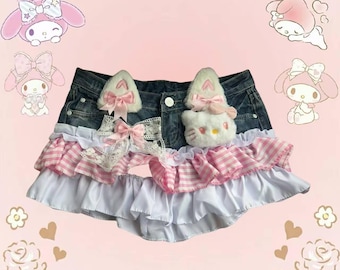 May include: Denim shorts with pink and white ruffles, lace, and bows. The shorts feature plush cat ears and a Hello Kitty face. The background is pink with the word "MEOW" and cartoon characters.