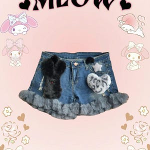 Pode incluir: Shorts de ganga azul com guarnição de pele cinzenta, com um coelho preto e uma aplicação de pelúcia em forma de coração cinzento.