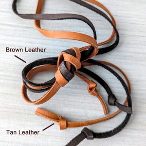 May include: Close-up of three leather cords, one black, one brown, and one tan. The cords are tied together in a knot. The text "Brown Leather" and "Tan Leather" are written on the image.