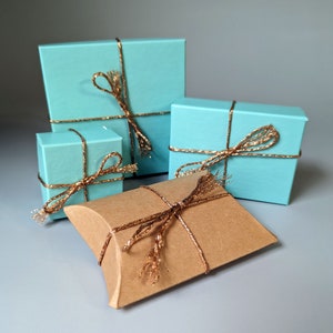 May include: Four gift boxes wrapped in light blue paper with gold ribbon. The boxes are arranged in a pyramid shape. The top two boxes are square, the bottom left box is square, and the bottom right box is a rectangular pillow box.