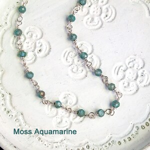 May include: A delicate silver chain necklace with moss aquamarine beads. The necklace is on a white background with a floral pattern.
