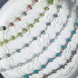 May include: Five delicate silver chains with different colored gemstones. The chains feature small, faceted gemstones in shades of green, blue, and pink.