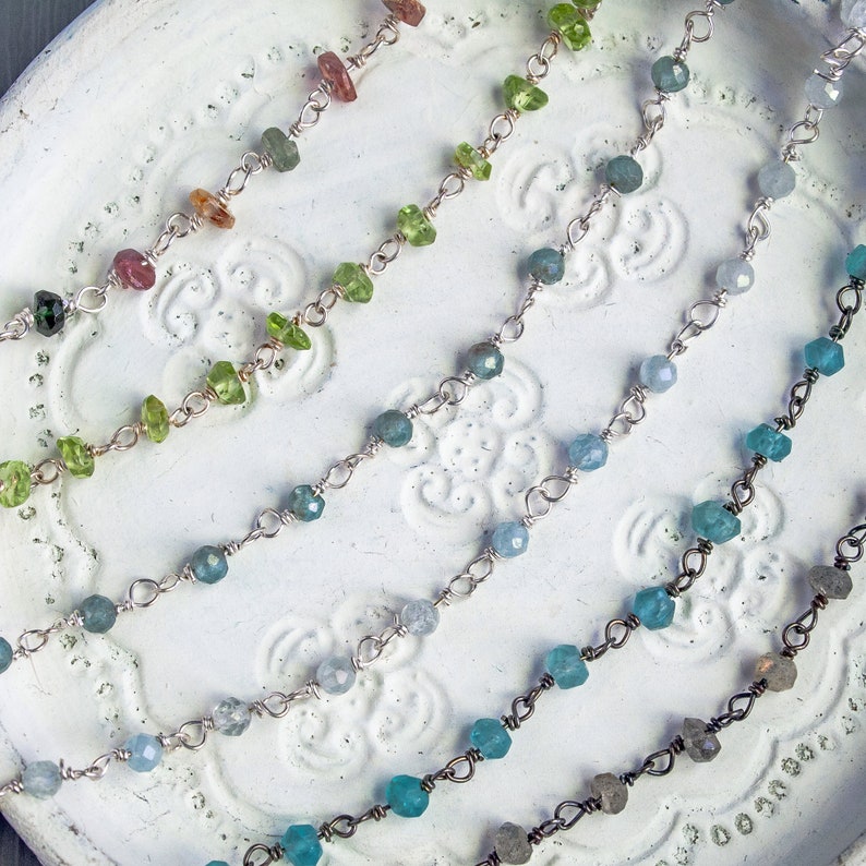 May include: Five delicate silver chains with different colored gemstones. The chains feature small, faceted gemstones in shades of green, blue, and pink.