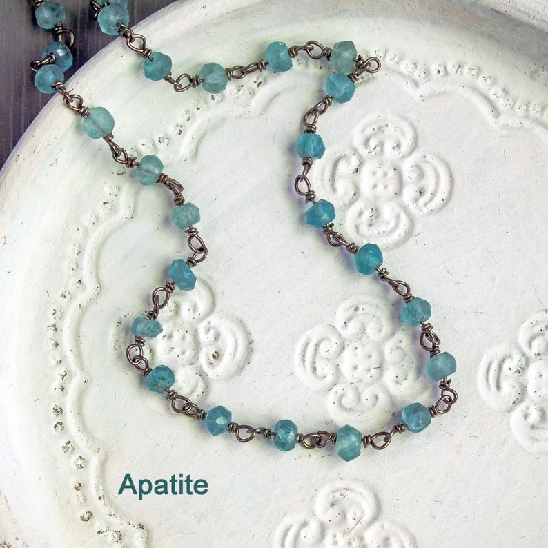May include: A delicate necklace made with light blue apatite beads and copper wire. The necklace is displayed on a white background with a floral design.