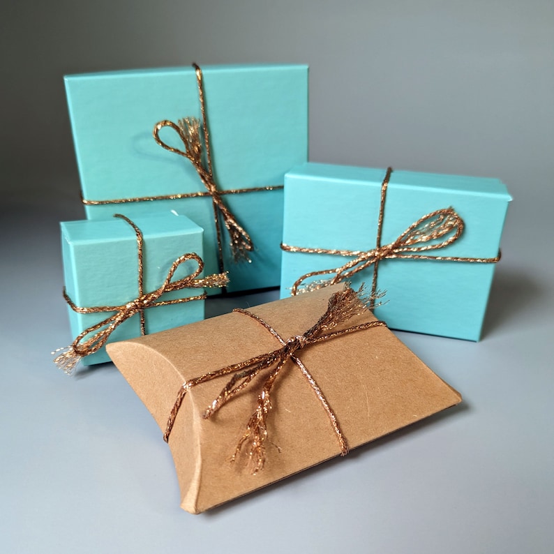 May include: Four gift boxes wrapped in light blue paper with gold ribbon. The boxes are arranged in a pyramid shape. The top box is the largest and the bottom box is the smallest. A brown gift box with gold ribbon is in front of the blue boxes.