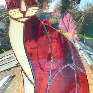 May include: A stained glass cat figurine with a white face and red body. The cat is sitting on a red base with the word "Mike" written on it.