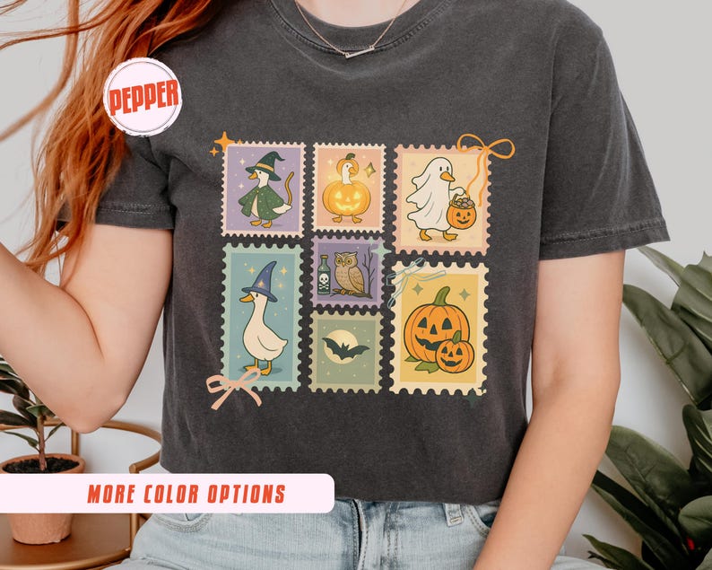 May include: Dark gray t-shirt featuring six postage stamp designs with Halloween-themed illustrations. The stamps depict a witch duck, a pumpkin, a ghost, a duck with a witch hat, an owl, and a pumpkin with a smaller pumpkin. The shirt has the word "Pepper" in a circle.