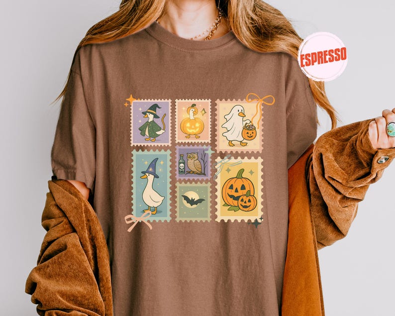 May include: Brown t-shirt featuring a collection of Halloween-themed postage stamp designs. The stamps depict a witch duck, a pumpkin, a ghost with a pumpkin bucket, a duck with a witch hat, an owl, a bat, and a jack-o'-lantern.