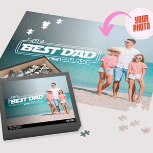 May include: A 1000 piece jigsaw puzzle with a photo of a family on a beach. The puzzle box shows a photo of the family with the text "The Best Dad in the Galaxy".