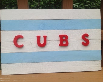 May include: A wooden sign painted in white and light blue stripes with the word "CUBS" spelled out in red letters.