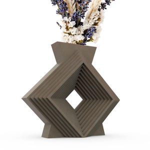 Könnte beinhalten: Eine geometrische, braune Keramikvase mit einer quadratischen Öffnung und einem geschichteten, gestapelten Design. Die Vase ist mit getrocknetem Lavendel und weißen Blumen gefüllt.