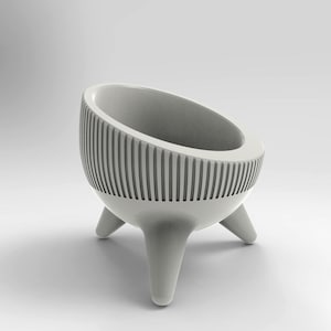 Puede incluir: Un macetero de cerámica blanco con un diseño acanalado y tres patas. El macetero está diseñado para contener una planta pequeña o una suculenta.
