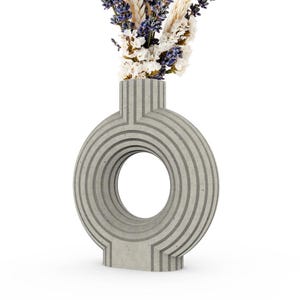 May include: A gray ceramic vase with a circular opening and a textured surface. The vase has a unique design with vertical lines and a ring-like shape.
