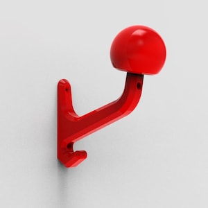 Puede incluir: Un gancho de pared rojo con una parte superior redondeada, con forma de hongo. El gancho está hecho de plástico y tiene un diseño simple.