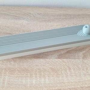 May include: A grey and white ceramic incense holder with a round, grey top. The holder has a series of grooves on the top and a white base.