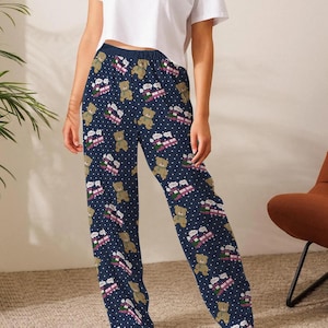 May include: Navy blue pajama pants with a repeating pattern of teddy bears, pink and white gift boxes, and white polka dots. The pants are worn with a white crop top. The pajama pants are made of a soft, comfortable material.