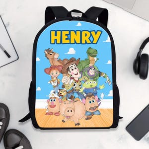 Pode incluir: Uma mochila preta com fundo azul com a palavra "HENRY" em amarelo. A mochila tem um gr&aacute;fico colorido de personagens do filme Toy Story. A mochila &eacute; cercada por t&ecirc;nis pretos, um caderno, um laptop, fones de ouvido e um smartphone.