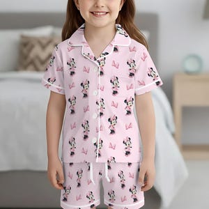 May include: Pink pajama set featuring a Minnie Mouse pattern. The short-sleeved top and shorts have white trim and a drawstring waist. The Minnie Mouse print includes bows and the character in a repeating pattern.
