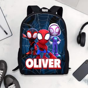 May include: Black backpack featuring Spider-Man characters with a web design background. The backpack has a large graphic of three characters and the name "OLIVER" in red and white. Includes adjustable straps.