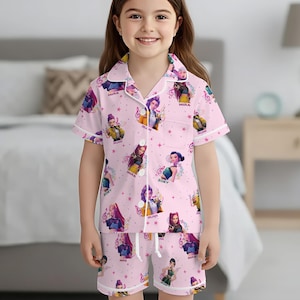 Peut inclure: Ensemble de pyjama rose avec un motif r&eacute;p&eacute;t&eacute; de personnages de dessins anim&eacute;s, de notes de musique et d'&eacute;toiles. Le haut &agrave; manches courtes et le short ont une bordure blanche. L'ensemble de pyjama est port&eacute; par une jeune fille.