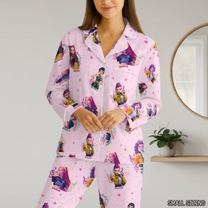 May include: Pink pajama set with a repeating pattern of cartoon characters, musical notes, and stars. The set includes a button-down top with white trim and matching pants. The text "SMALL SIZING" is visible.