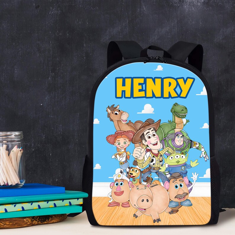 Pode incluir: Mochila preta com um painel frontal azul com o nome "HENRY" em letras amarelas. O painel exibe personagens de desenhos animados do filme Toy Story. A mochila tem al&ccedil;as pretas e uma parte traseira preta.