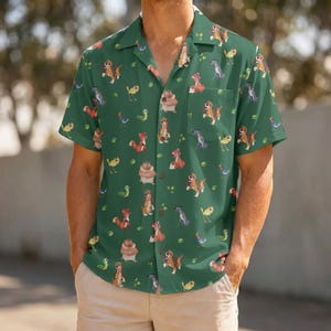 May include: A short-sleeved button-down shirt in a deep forest green color featuring an all-over repeating pattern of various cartoon animals including dogs, birds, and caterpillars. The shirt has a classic collar and a single chest pocket.