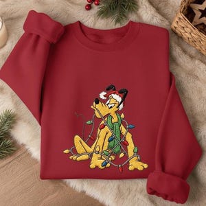 Pode incluir: Um moletom vermelho com um cachorro de desenho animado bordado usando um gorro de Papai Noel e um cachecol verde, enroscado em luzes de Natal. O moletom tem punhos e gola redonda.