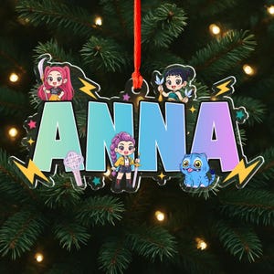 May include: A personalized Christmas ornament with the name "ANNA" in large, colorful letters. The ornament features cartoon characters and lightning bolt accents. It hangs from a red ribbon, perfect for holiday decor.