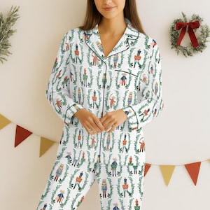 May include: White pajama set with a festive print of nutcrackers, mice, and green garland. The long-sleeved top and pants have black trim. A Christmas-themed pajama set.