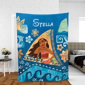 May include: A blue fleece blanket featuring a graphic of the character Moana centered within a triangular frame. The design includes the name Stella in white script, stylized ocean waves, tropical flowers, and geometric patterns in shades of blue, orange, and yellow.