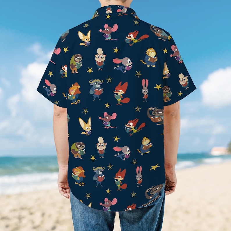 Puede incluir: Una camisa de manga corta azul oscuro con un patr&oacute;n repetitivo de varios animales de dibujos animados, incluyendo zorros, conejos y ratones, cada uno sosteniendo un libro, intercalados con peque&ntilde;as estrellas amarillas en la tela.