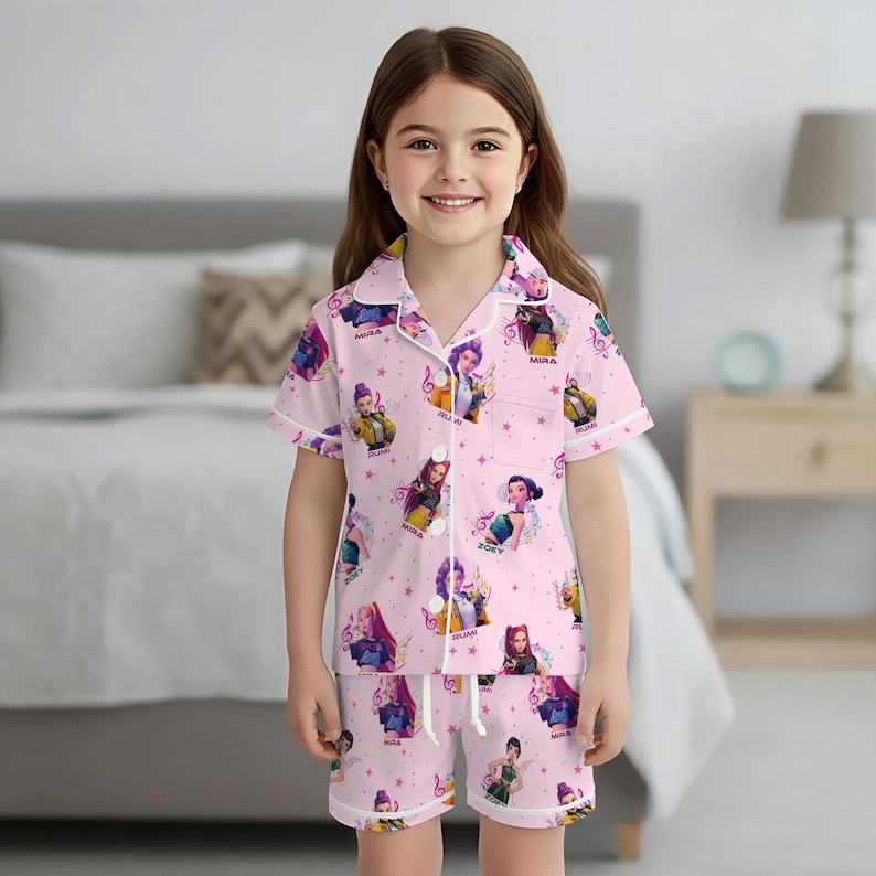 Peut inclure: Ensemble de pyjama rose avec un motif r&eacute;p&eacute;t&eacute; de personnages de dessins anim&eacute;s, de notes de musique et d'&eacute;toiles. Le haut &agrave; manches courtes et le short ont une bordure blanche. L'ensemble de pyjama est port&eacute; par une jeune fille.