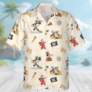 May include: Cream-coloured button-down shirt featuring a repeating pattern of cartoon pirate characters, treasure maps, and nautical elements. The characters include Mickey Mouse, Minnie Mouse, Donald Duck, and Pluto. The shirt has short sleeves and a classic collar.