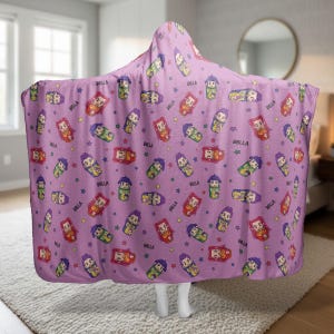 May include: A hooded blanket in a lavender color, patterned with cartoon illustrations of a character and the word "BELLA". The design includes colorful stars and repeated images of the character in various poses.