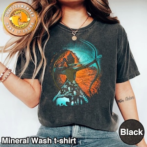 Puede incluir: Una camiseta negra de algodón lavado con un estampado gráfico de una mujer con arco y flecha. El gráfico está rodeado de un círculo con el texto "Crafts 4 Wonder Make It Yours". El gráfico también incluye un oso y follaje.