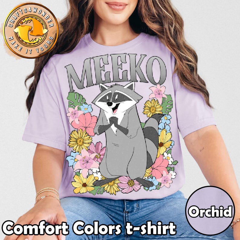 Pu&ograve; includere: T-shirt Comfort Colors color orchidea con un procione dei cartoni animati di nome Meeko, circondato da fiori colorati. La parola "MEEKO" &egrave; stampata sopra il procione in lettere grigie. La maglietta ha maniche corte.