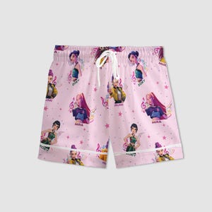 Peut inclure: Un short de pyjama rose avec un motif r&eacute;p&eacute;t&eacute; de femmes de dessins anim&eacute;s, de notes de musique et d'&eacute;toiles. Le short a un cordon de serrage blanc et une bordure blanche. Les noms "Zoey", "Mira" et "Rumi" sont visibles.