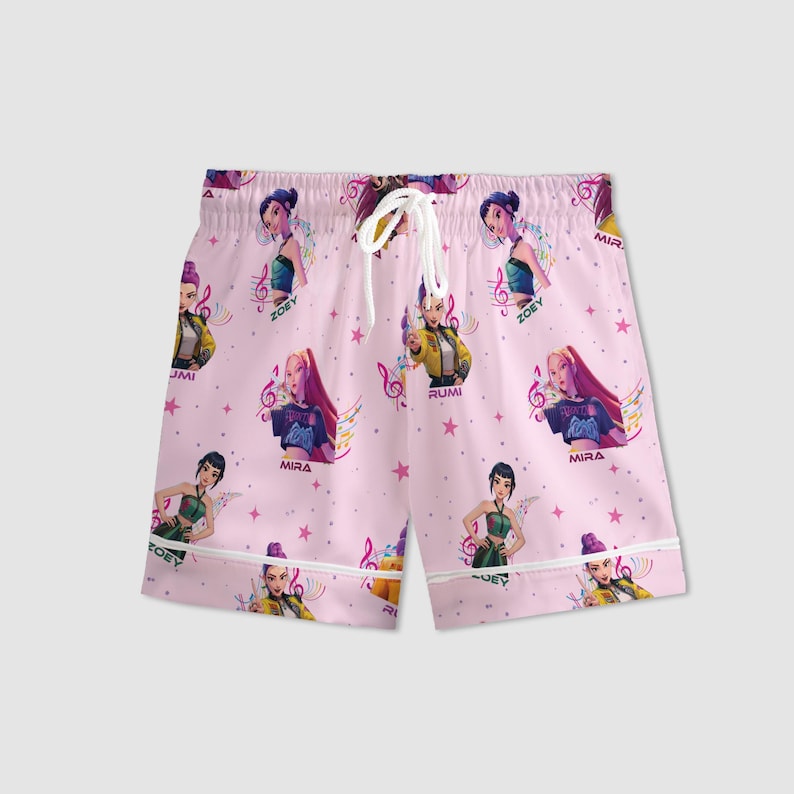 Peut inclure: Un short de pyjama rose avec un motif r&eacute;p&eacute;t&eacute; de femmes de dessins anim&eacute;s, de notes de musique et d'&eacute;toiles. Le short a un cordon de serrage blanc et une bordure blanche. Les noms "Zoey", "Mira" et "Rumi" sont visibles.