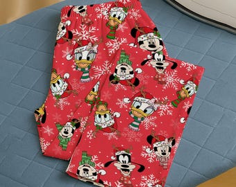 May include: Red Christmas-themed pajama pants featuring Mickey Mouse, Minnie Mouse, Donald Duck, and Goofy in festive attire. The pants have a repeating pattern of the characters, snowflakes, and holiday accessories.