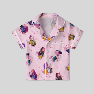 Peut inclure: Haut de pyjama rose &agrave; manches courtes avec un motif r&eacute;p&eacute;t&eacute; de personnages anim&eacute;s, de notes de musique et d'&eacute;toiles. Le haut a une bordure blanche et une poche poitrine. Les noms "MIRA", "RUMI" et "ZOEY" sont imprim&eacute;s.