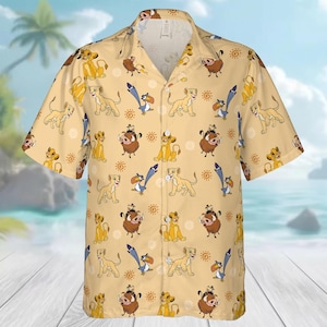 Könnte beinhalten: Ein kurzärmeliges Hemd mit hellgelbem Hintergrund. Das Hemd hat ein sich wiederholendes Muster von Zeichentrickfiguren, darunter Löwen, Warzenschweine und Vögel. Das Design beinhaltet sonnenähnliche Formen. Das Hemd hat einen klassischen Kragen und eine lockere Passform.