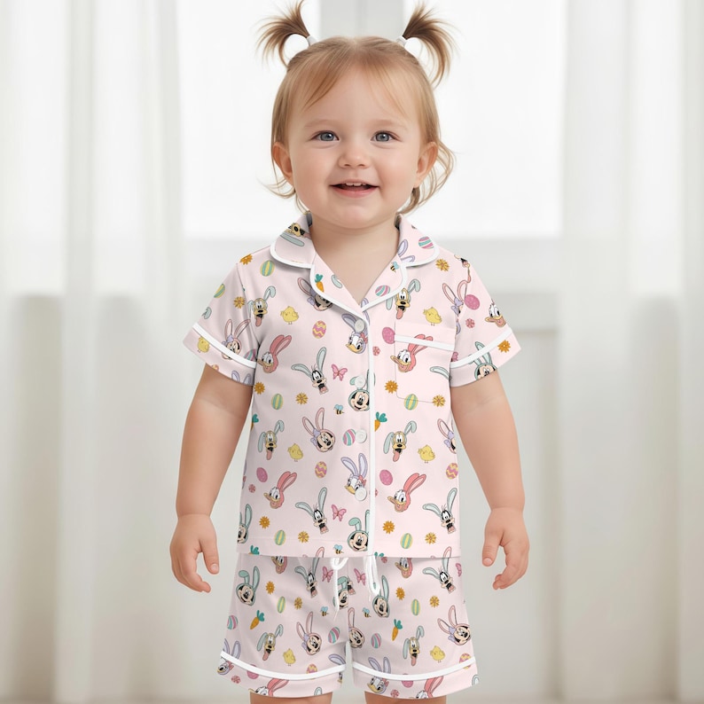 Puede incluir: Conjunto de pijama rosa claro con un estampado de conejitos de dibujos animados, huevos de Pascua y flores. La parte superior de manga corta y los pantalones cortos tienen ribetes blancos. El pijama est&aacute; hecho de una tela suave y ligera.