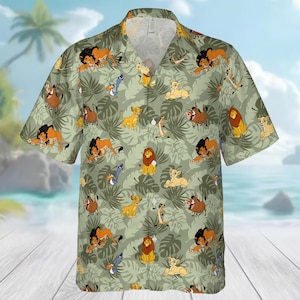 Può includere: Camicia a maniche corte con bottoni e un motivo ripetuto di personaggi de Il Re Leone, tra cui leoni, Timon, Pumbaa e Zazu, su uno sfondo verde chiaro con foglie tropicali. La camicia ha un colletto classico e una vestibilità rilassata.